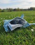 Ein grüner Wetbag mit weissen Punkten liegt auf einer Wiese mit Gänseblümchen im Sonnenschein