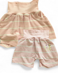 Bunte, kurze Kinderhose aus upgecycelten Stoffen hier aus einem Poloshirt mit elastischem Bund, nachhaltig hergestellt und ideal zum Spielen und Toben. Farbe Rosa-Weiss-gestreift mit rosa Bund und blümchen Stickerei hinten.