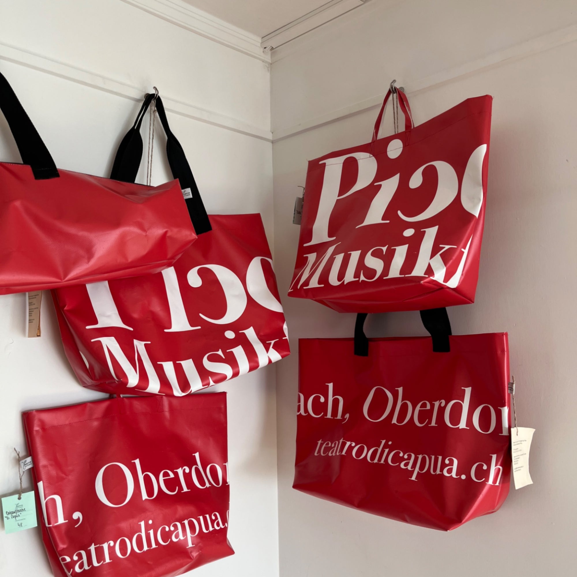 Verschiedene rote upcycling Blachentaschen hängen an einer weissen Wand