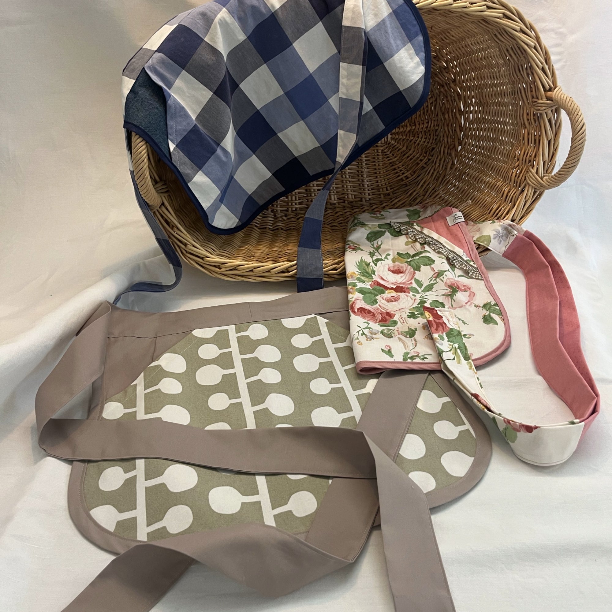 Drei ganz verschiedene Chlüpplischürzen liegen bei einem Weidenkorb