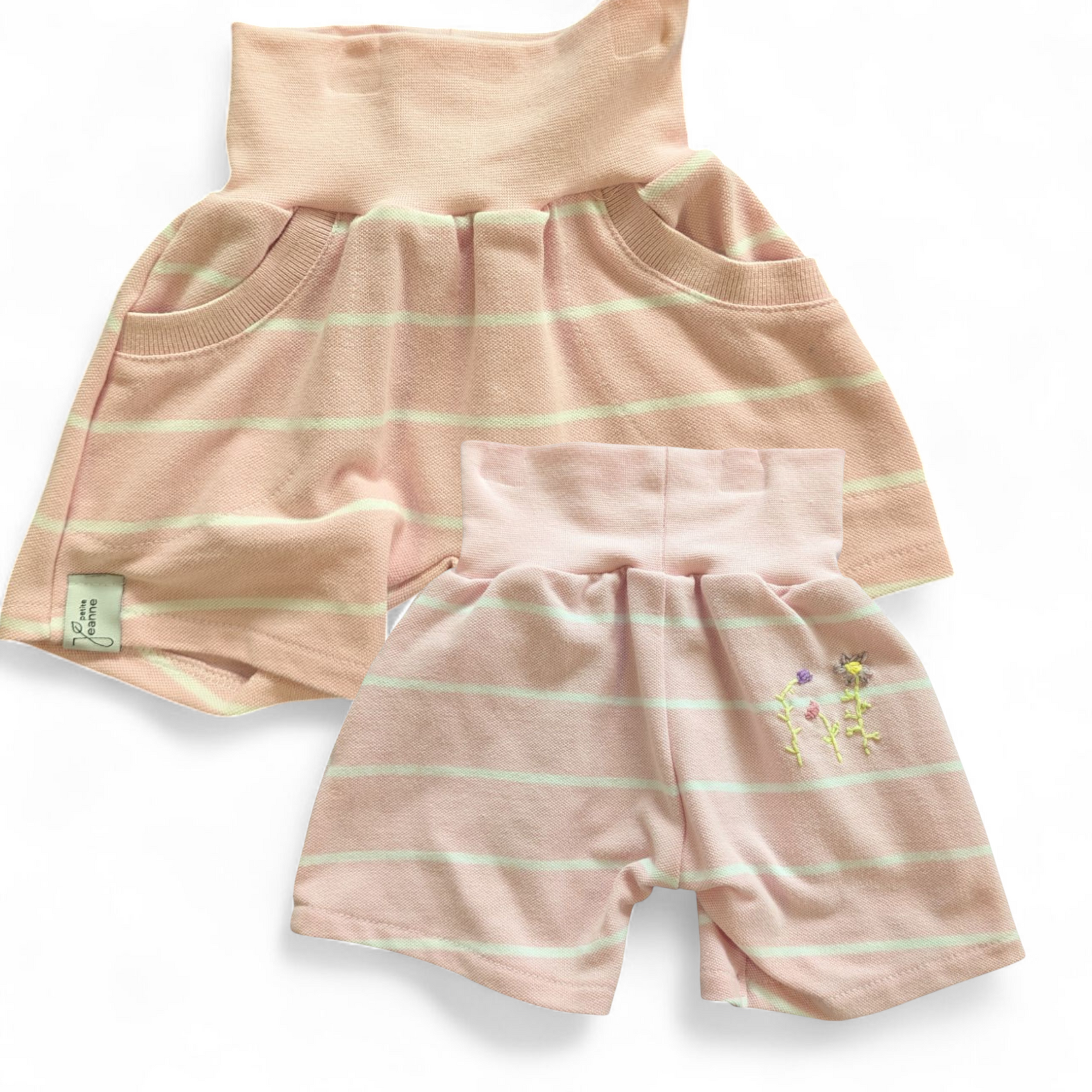 Bunte, kurze Kinderhose aus upgecycelten Stoffen hier aus einem Poloshirt mit elastischem Bund, nachhaltig hergestellt und ideal zum Spielen und Toben. Farbe Rosa-Weiss-gestreift mit rosa Bund und blümchen Stickerei hinten. 