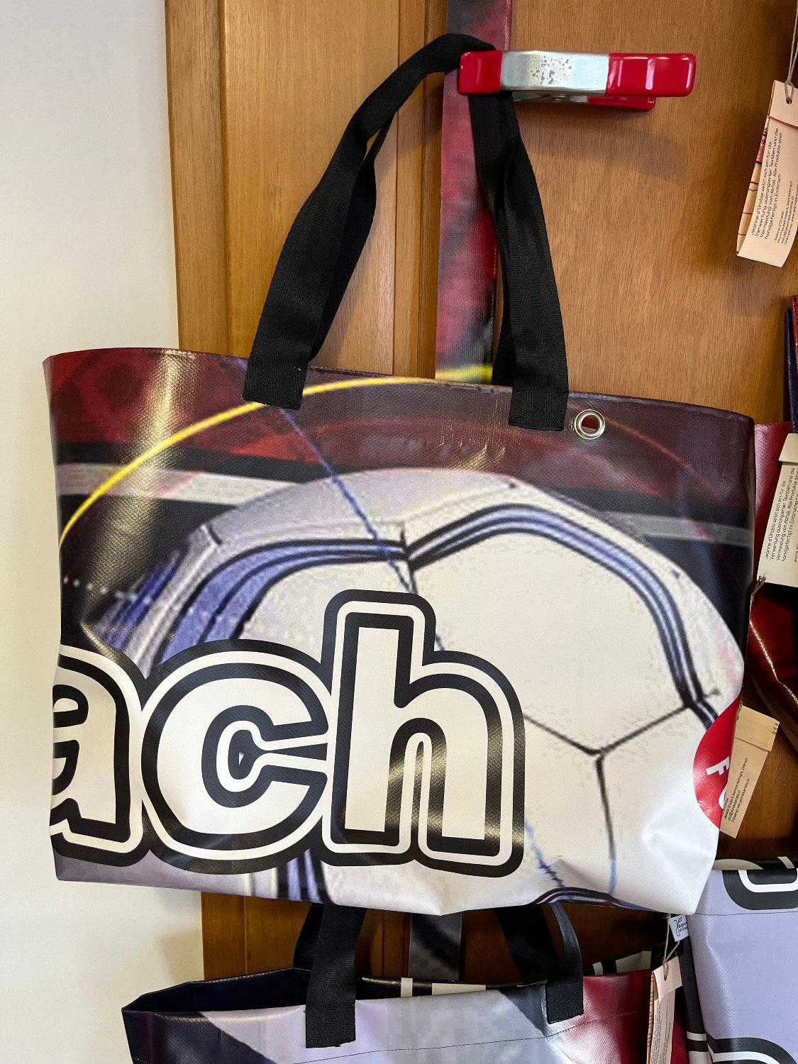 Eine Upcycling-Tasche aus Werbeblache hängt vor einer Holztüre