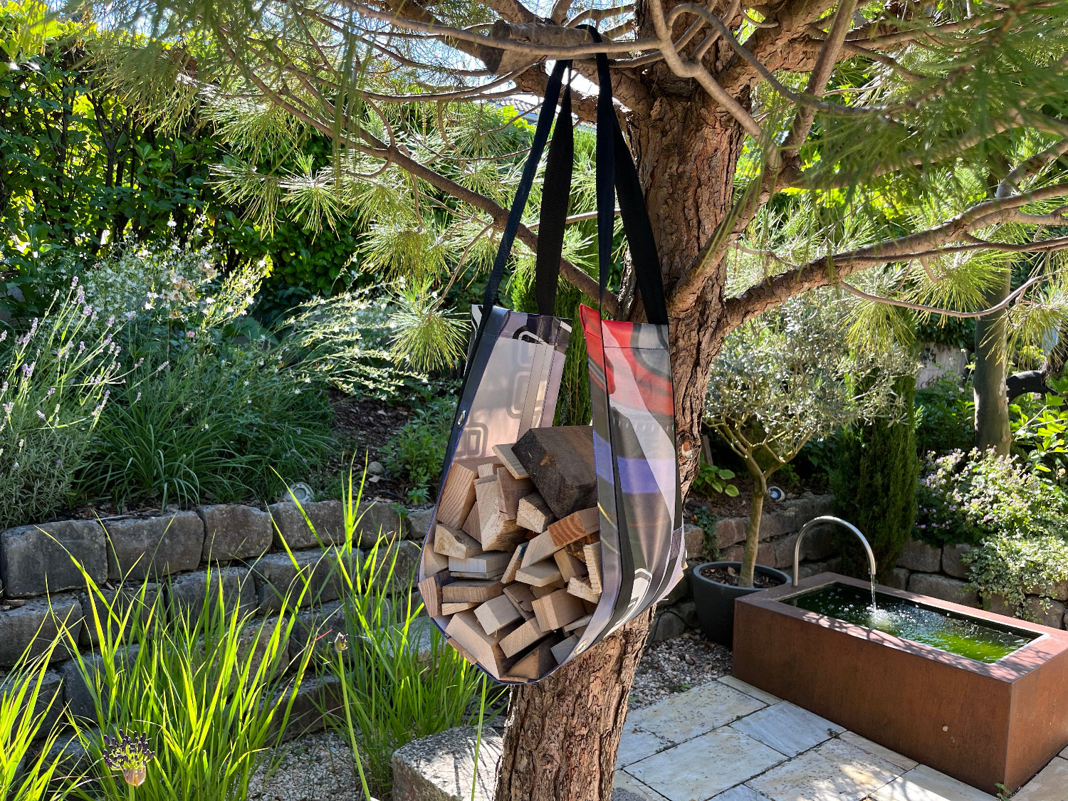 Eine Transporttasche für Kaminholz hängt an einem Nadelbaum