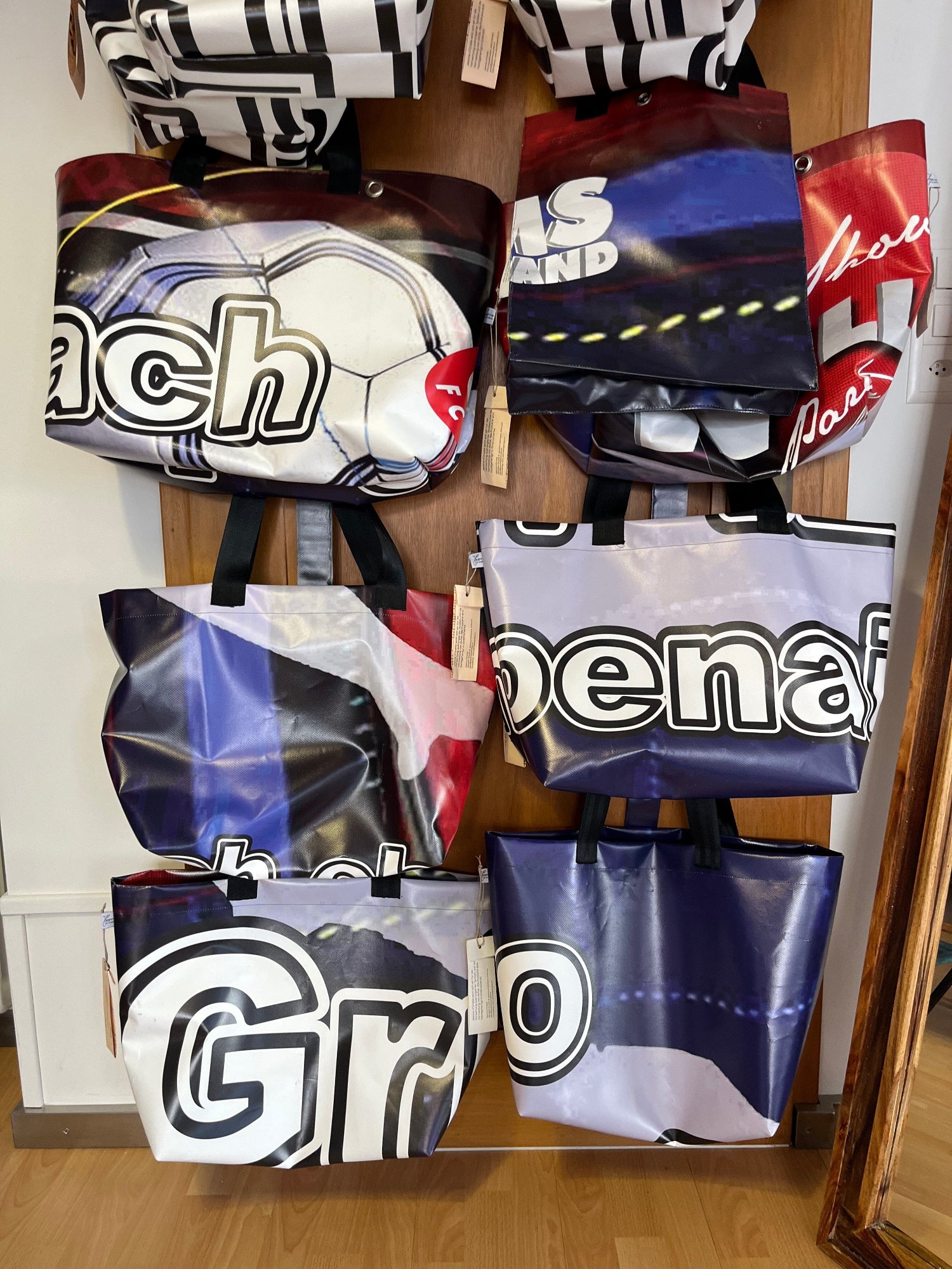 Verschiedene Upcycling-Taschen aus Werbeblachen hängen an einer Holztüre